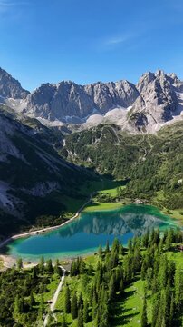 Vertical aerial drone view of the Alps and the green Seebensee on a sunny summer day. A couple enjoys the view of Seebensee and goes hiking. Seebenlake