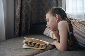 A girl comfortably lying on a sofa, engrossed in reading a book, depicting relaxation and quiet leisure
