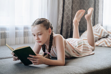 A girl comfortably lying on a sofa, engrossed in reading a book, depicting relaxation and quiet leisure