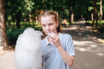 A joyful girl in a park happily eating cotton candy, capturing a moment of childhood delight and outdoor fun