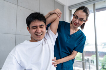 Obraz premium Young asian man patient undergoes chiropractic physical therapy under the supervision of a smiling woman physical therapist in a physical therapy clinic.