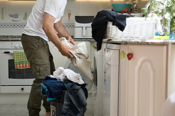 A white man doing laundry in his kitchen at home.