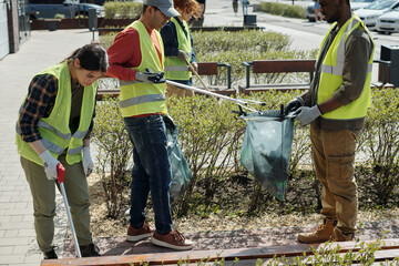 Diverse group of young adult and middle aged men and women wearing safety vests cleaning park area...