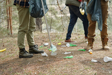 Group of young adult men cleaning forest floor, picking up plastic bottles and trash with grabbers...