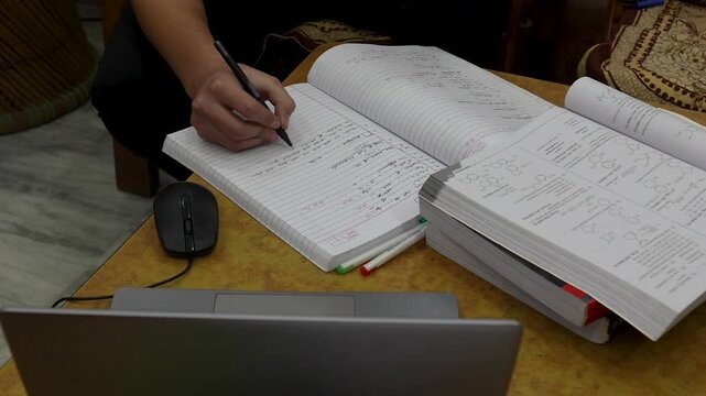 Indian student writing notes at night with books and laptop for intense study