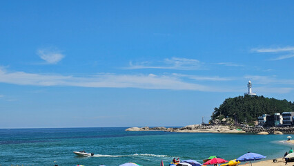 Obraz premium 강원도 속초 해수욕장과 등대, 파라솔과 보트가 있는 여름 바다 풍경