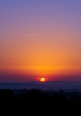 Fototapeta premium Sunset Scene with Bright Orange Sun Setting Over Mountain Horizon in Clear Sky