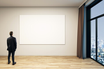 Businessman observing empty white canvas in modern gallery interior with city view through window...