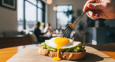 Hand piercing a perfectly cooked fried egg on avocado toast with runny yolk
