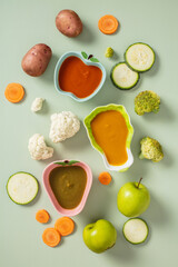 Assorted vegetables and colorful purees in fruit-shaped bowls on a light green background. Ideal for themes of children's nutrition, healthy eating, baby food, and meal preparation.