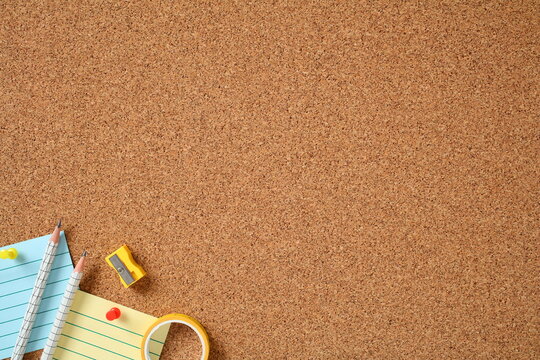 Pencils, sticky notes, sharpener, and push pins arranged on corkboard. Back to school concept,