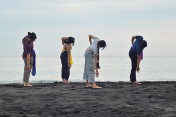 The group of girls gently leans to the right in synchronized yoga motion, stretching one arm...
