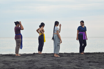 One of the girls steps forward and resumes leading their beach yoga session while others watch...