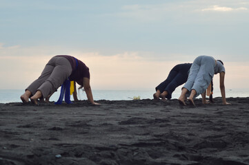 On the quiet beach, four girls lean back on their hands, stretching their legs behind while facing...