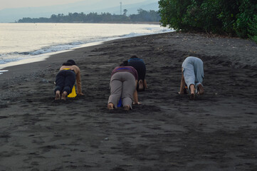 Captured from the back, four girls in beachwear perform a yoga pose leaning on their hands with...
