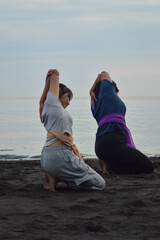 With focused expressions, two teenage girls mirror each other in a yoga pose leaning left, knees...