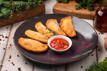 Fried empanadas served with spicy tomato dip on dark plate
