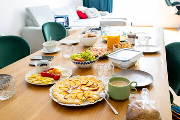 charming rustic peach tart is the focal point of a beautifully arranged wooden brunch table, surrounded by fresh fruits, cheeses, and warm beverages. Bathed in soft natural light