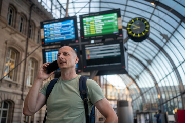 Businessman using mobile phone while walking with luggage at train station on business trip