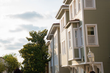Traditional Turkish Ottoman houses with distinct bay windows and light green facades under a bright, cloudy sky. Row of historic wooden houses in a charming neighborhood. Residential architecture