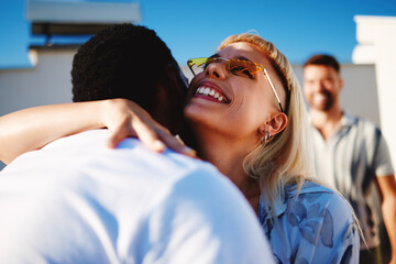 Woman with sunglasses hugging a man on a rooftop enjoying a sunny day with friends