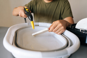 Person using steam cleaner for sanitizing humidifier filter submerged in basin of water, promoting clean and healthy air for improved indoor air quality and wellness. Concept of hygiene, cleanliness.