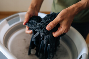 Cropped shot of unrecognizable person soaking black laundry in water in folding basin standing at...