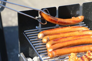 close-up of a bratwurst being turned onto the grill with tongs