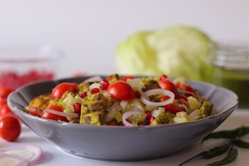 grilled paneer cubes, cherry tomatoes, pomegranate seeds, sliced onions, and shredded lettuce in a gray bowl.