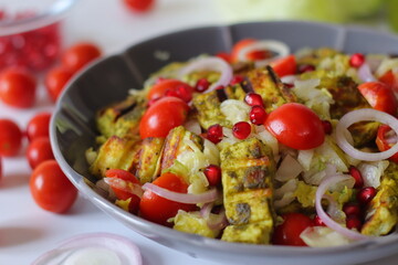 grilled paneer cubes, cherry tomatoes, pomegranate seeds, sliced onions, and shredded lettuce in a gray bowl.