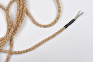 An electric cable with a braided natural fiber covering and exposed wires at one end is coiled on a white background