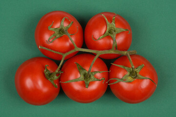 A cluster of five ripe, red tomatoes on the vine is vibrantly displayed against a dark green background