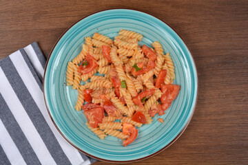 A delicious plate of fusilli pasta with tuna and fresh tomatoes is served on a rustic wooden table with a striped napkin