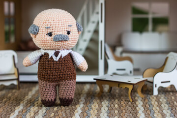 Crochet amigurumi grandpa toy near doll house on lawn, own home in retirement