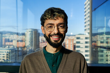 Headshot portrait of a confident man smiling to camera in a modern office.