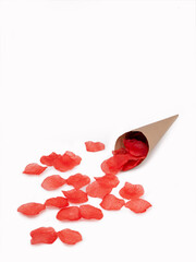 Paper bag with red rose petals over scattered petals on white background, space for text