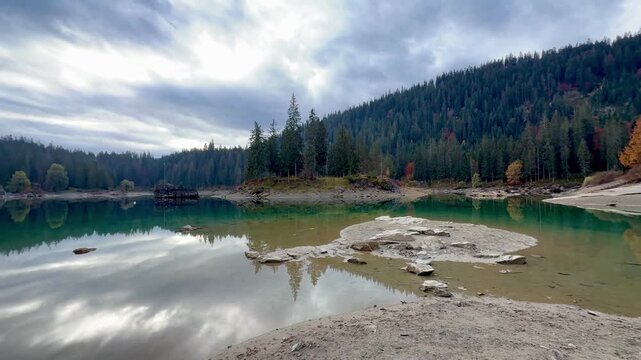 Lake Cauma with its crystal-clear, green water, which reflects the landscape on the calm surface of the water, framed by autumnal forests. Taken on an early morning without people at the lake.