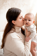 a mother with a baby, a mom holding her son's little child in her arms, hugging and kissing him, maternal love and care, mother and child