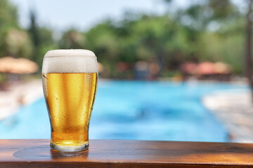 Glass of chilled beer on table and blurred pool water at the background. Place for your product or brand name display.