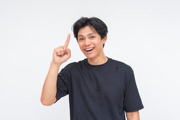 A happy young Asian man smiling with delight, confidently lifting one finger as if having a lightbulb moment. Isolated on a white background.