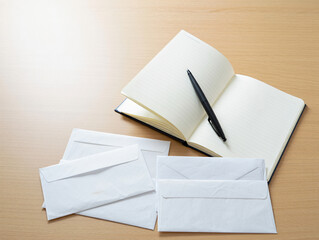 An open notebook with a pen lies near several white envelopes on a wooden desk