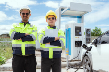 Two workers stand confidently at an electric vehicle charging station on a sunny day in a rural area
