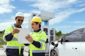 Electric vehicle charging experts discuss project details at a modern charging station in bright daylight