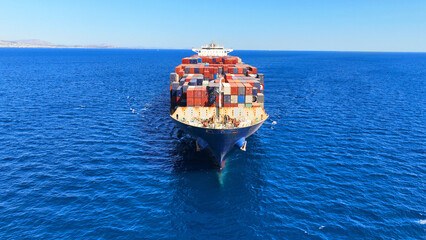 Aerial drone flight over colorful truck size container ship cruising in open ocean deep blue...