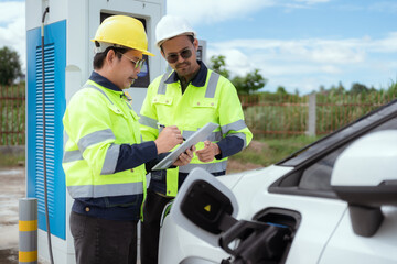 Engineers discuss electric vehicle charging station installation during sunny afternoon outdoors