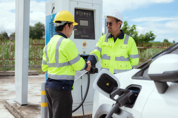 Two workers shake hands at an electric vehicle charging station in bright daylight during a workday