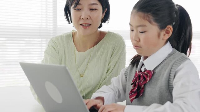 教室で女性教員からパソコンを教わる女の子