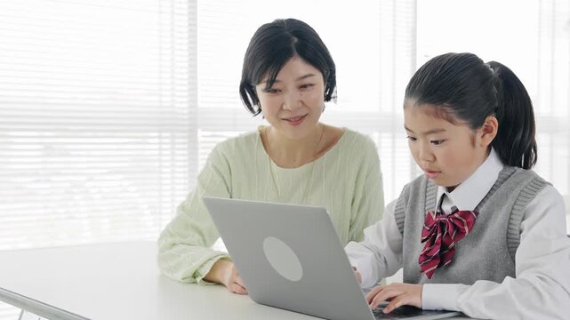 A girl learning how to use a computer from a female teacher in a classroom