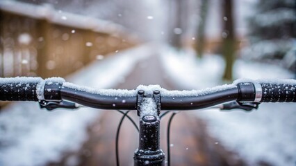 Snow-covered bicycle handlebars with a blurred wintery path and falling snowflakes in the background.