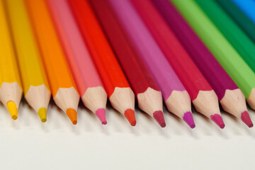 New wooden colored pencils of rainbow colors, perfectly sharpened, lie on table